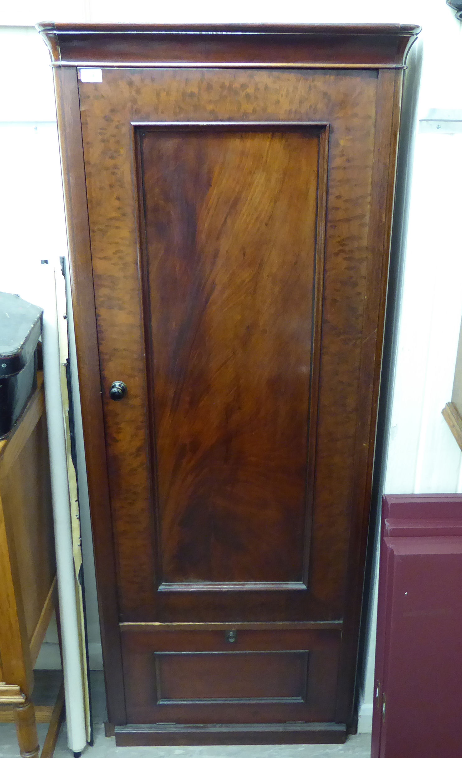 A late Victorian flame mahogany finished hallrobe with a moulded cornice, over a panelled door,