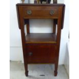 An Edwardian mahogany bedside table, the top with fall flaps over a drawer and a cupboard door,