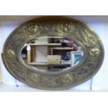 An early 20thC Arts & Crafts inspired mirror, the oval, bevelled plate set in a wide brass frame,