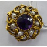 An 'antique' foliate scrolled, yellow metal circular brooch, set with an amethyst,
