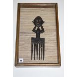 A large African tribal comb depicting a female figure, mounted in a frame.