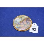 A yellow metal brooch with embroidered landscape within floral wreath border, 5.8cms wide.
