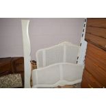 A cream painted double bedstead with caned head and foot boards, with shaped side panels,