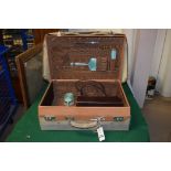 A leather suitcase with canvas cover; containing silver and guilloche enamel dressing table items,