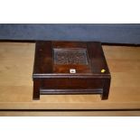 An Arts and Crafts box and cover with carved panel top and splay block supports, 38cms wide.