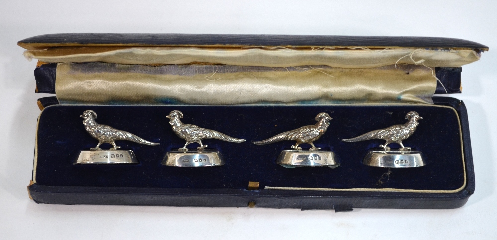 A cased set of four silver menu-card holders, cast with golden pheasants on weighted oval bases,