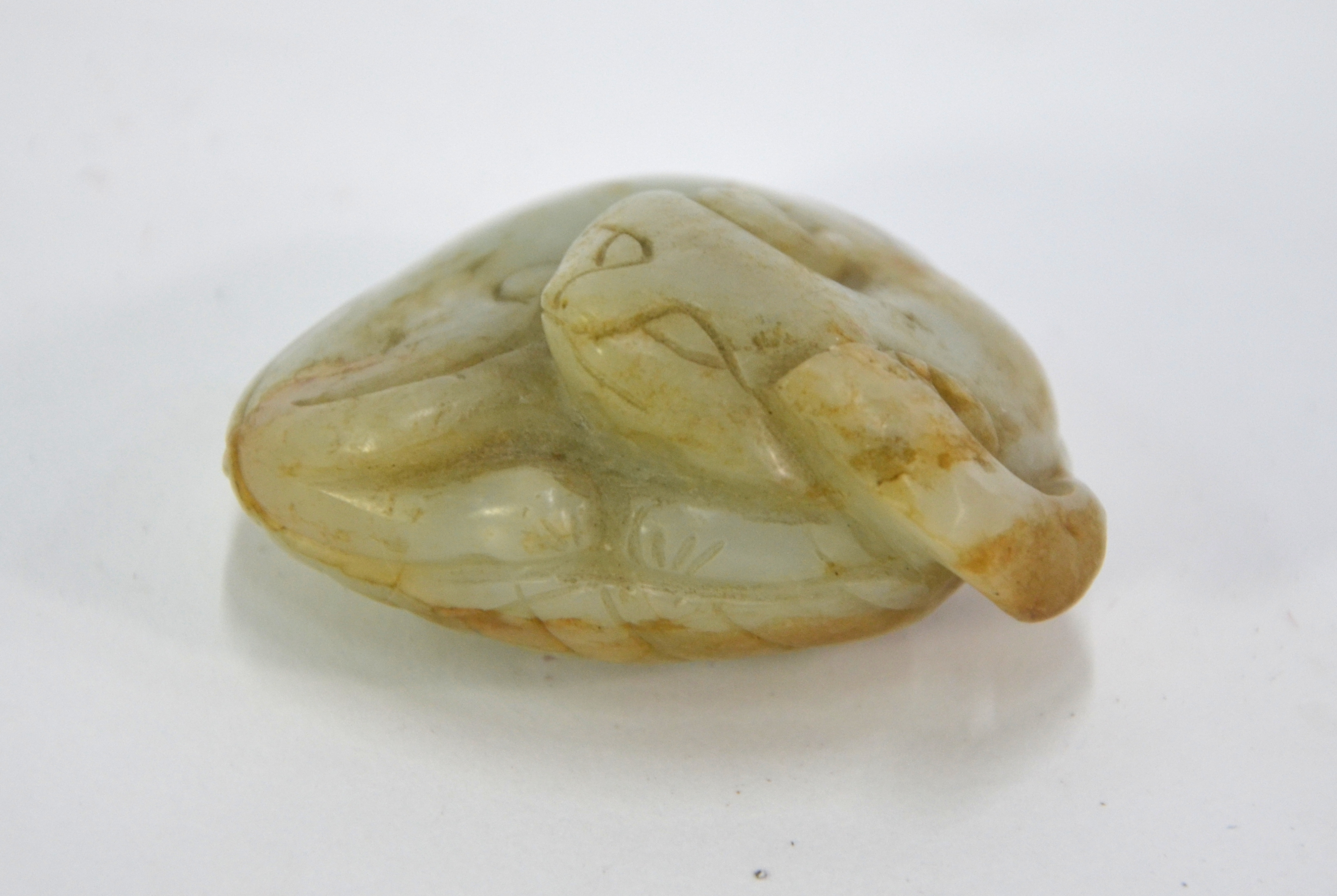 A mottled green jade carving of a coiled cat, curled up on a leaf, 5.5 cm long; post Qing Dynasty