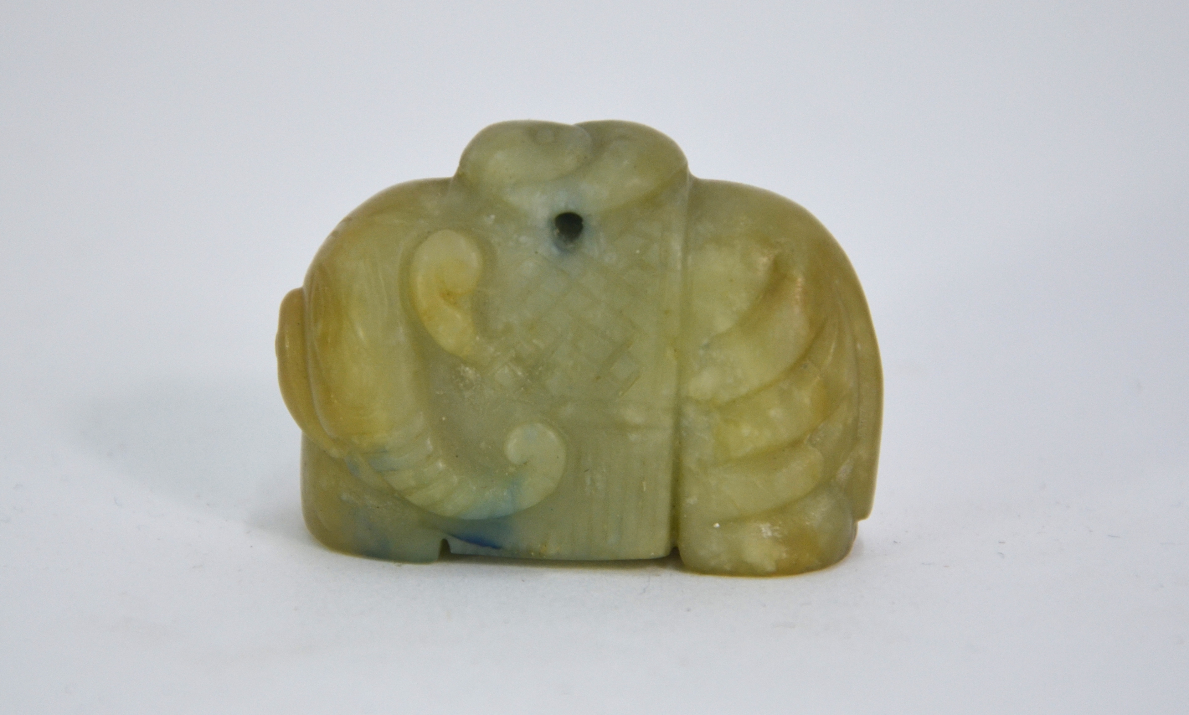 A mottled green stone figure of a standing elephant looking to the left and wearing a long howdah