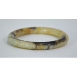 A mottled cream/grey jade bangle of circular form, carved on the exterior with a continuous