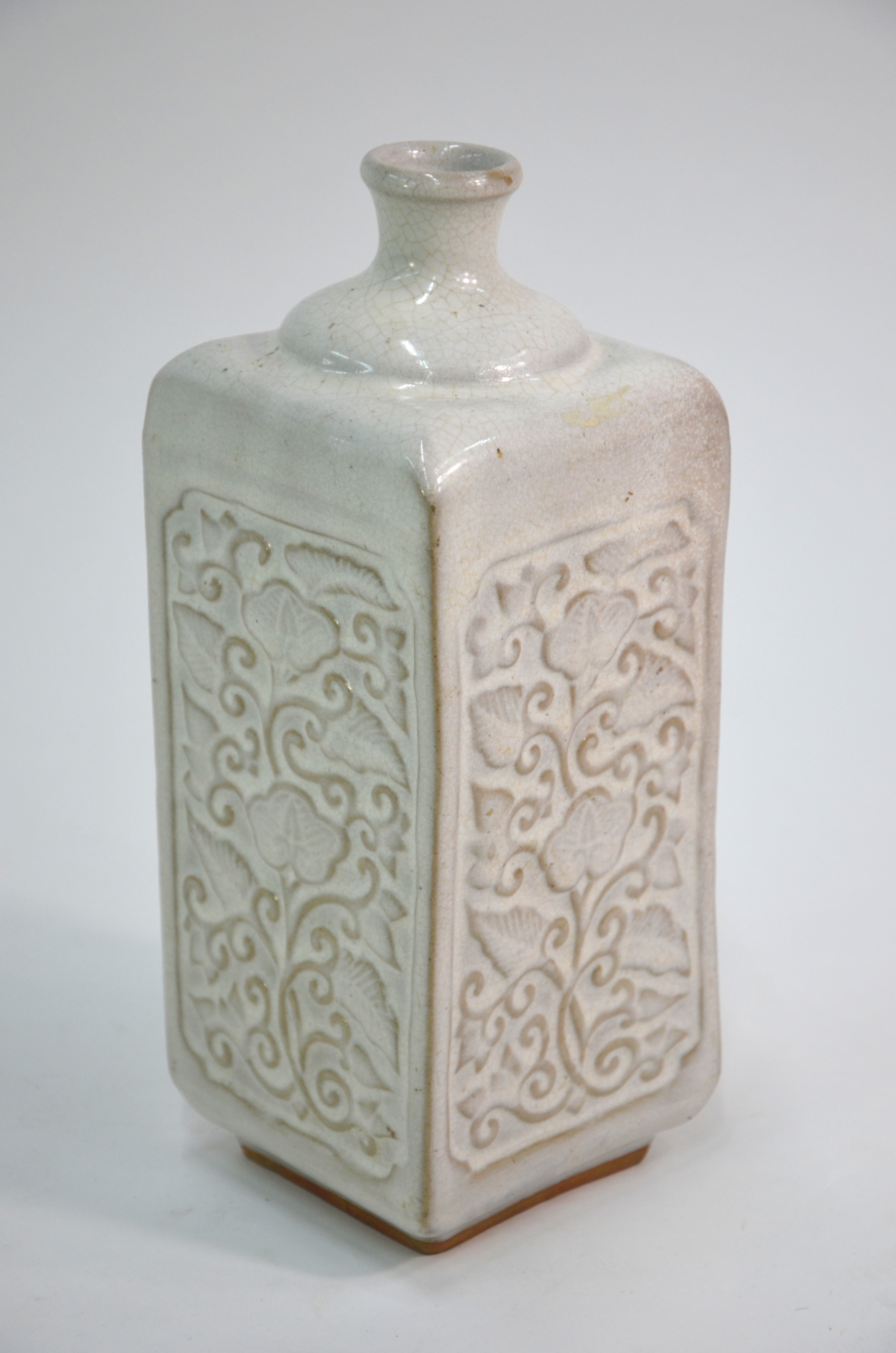 A cream-grey bottle vase of square section; decorated on each rectangular panel with carved floral