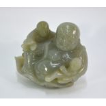 A green jade carved as Budai, seated on a large lotus leaf with two children, 7cm high, post Qing