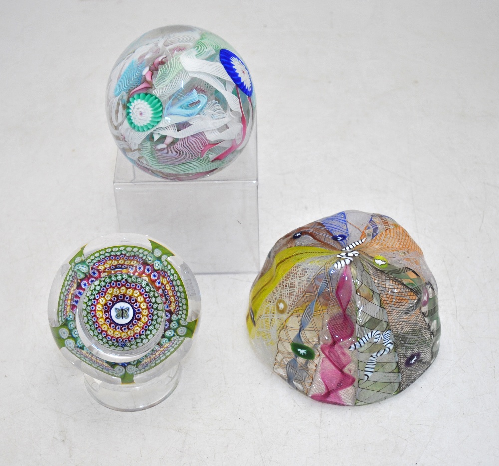 A faceted glass paperweight decorated with a central butterfly cane and concentric bands of canes in