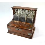 A brass mounted oak mirror-backed Tantalus with a trio of moulded glass decanters. the twin lidded