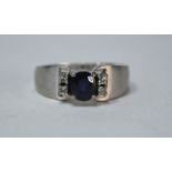 A contemporary style sapphire and diamond ring, set circular sapphire having two diamonds either