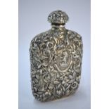 A US unmarked white metal hip flask, richly embossed with floral and foliate designs and with