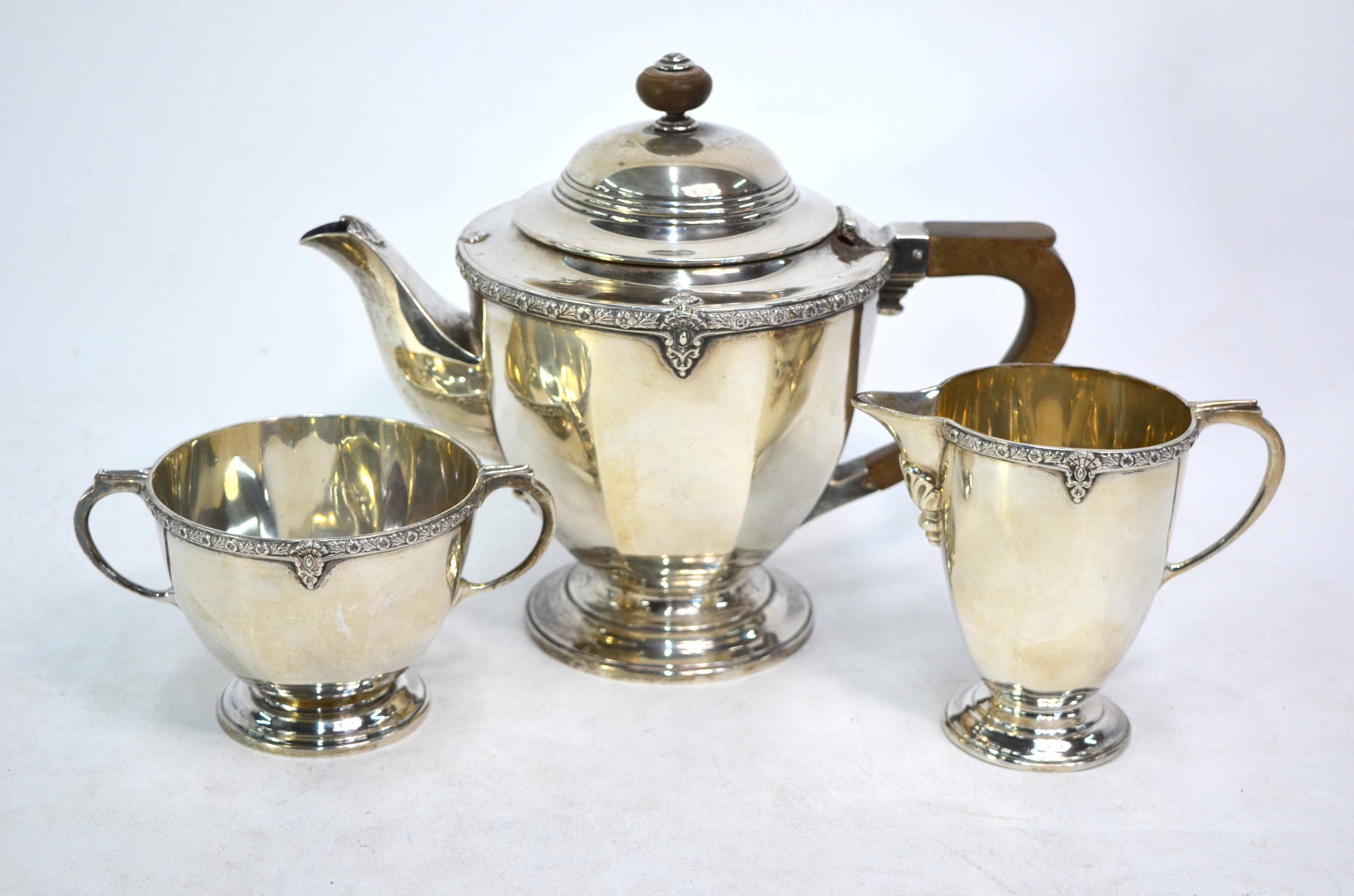 A three-piece silver tea service with floral-cast rim and moulded foot, composite handle and finial,