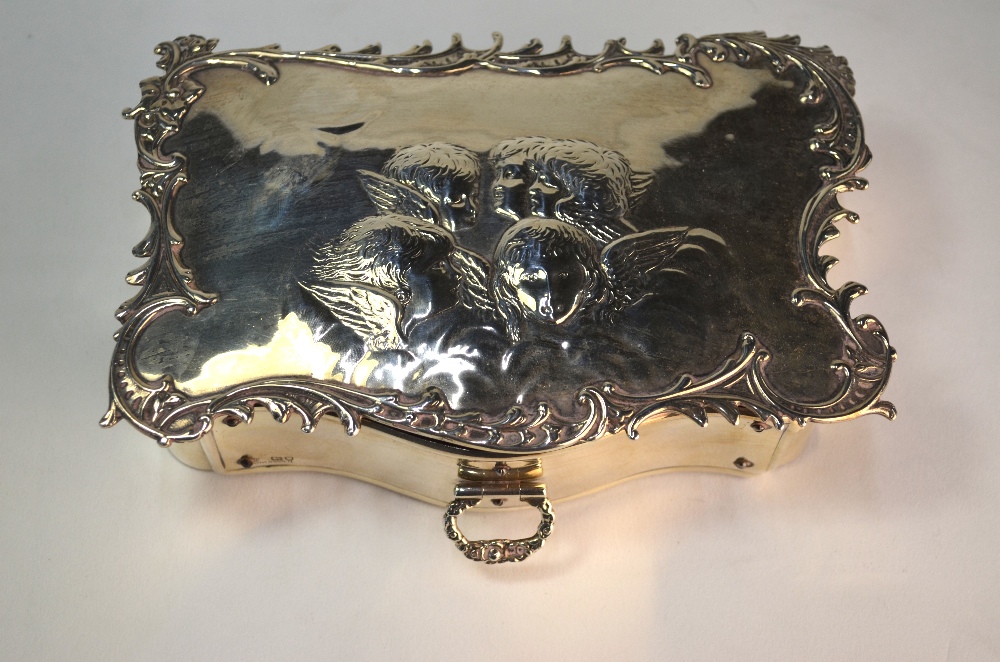 A silver jewellery box of serpentine form, the scroll-edge top embossed with winged cherub-heads,