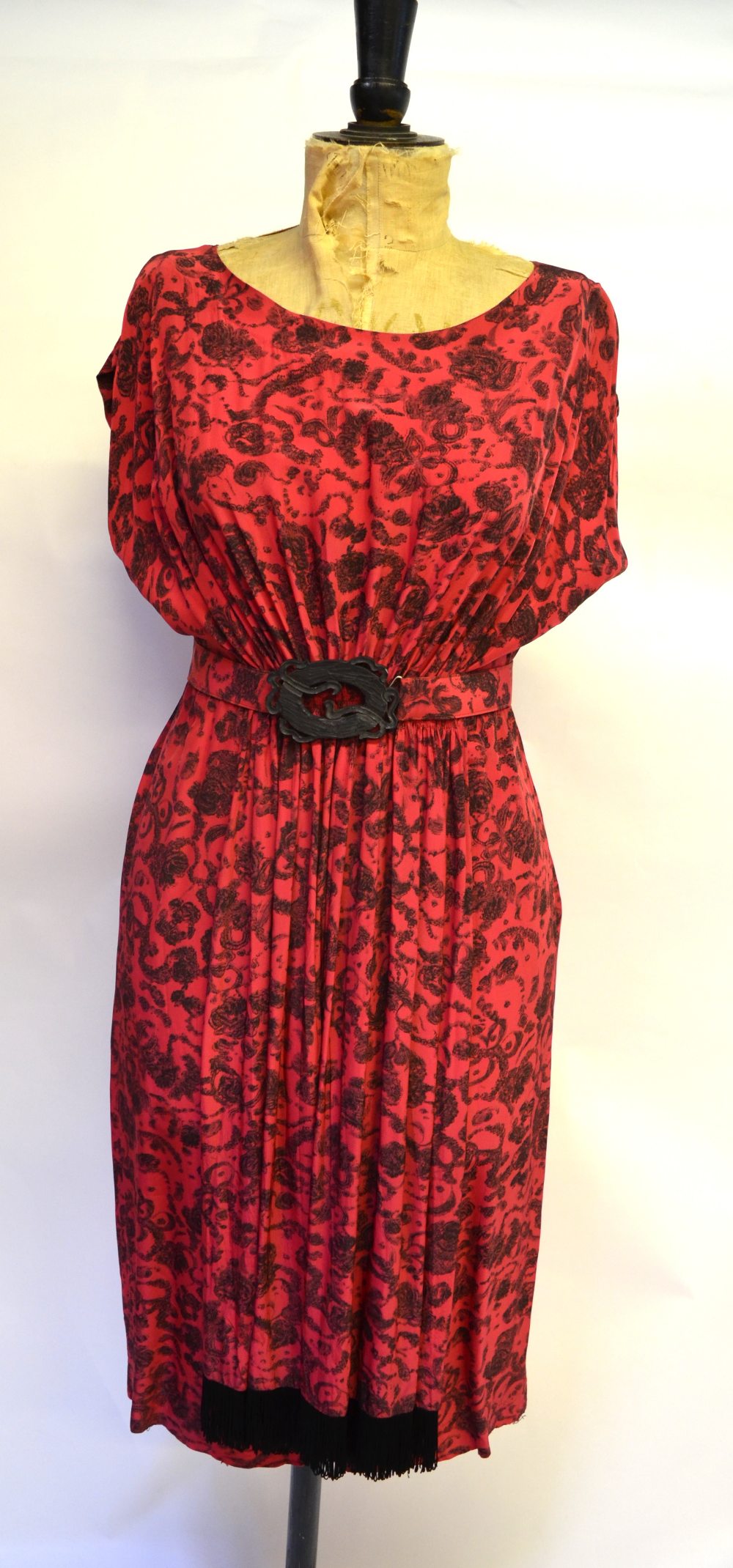 A 1940s red silk dress with black garland print, ruched waist falling to fringed drape, the belt