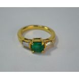 An emerald and diamond three stone ring, the central rectangular emerald having tapered baguette
