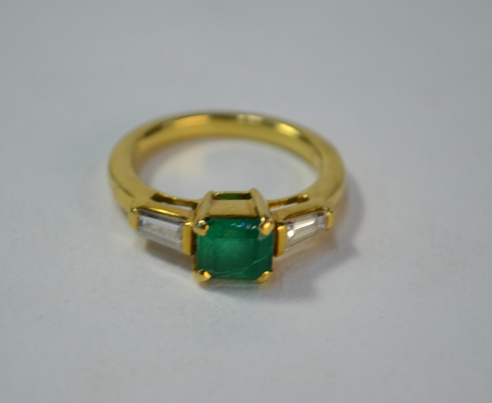 An emerald and diamond three stone ring, the central rectangular emerald having tapered baguette