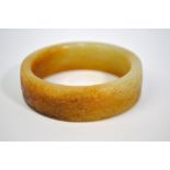 A Chinese modern, mottled jade bracelet of cylindrical form with russet inclusions, decorated with