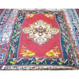 A Karabagh Kelim rug with large central floral medallion on red ground with stylized navy border 180