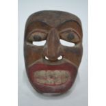 An ethnographic wood mask designed with black eye balls, red lips and white teeth, 20 cm high and