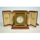 An Art Deco gilt metal and champlevee enamel travel clock with alarm, 6 cm high, in leather