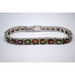 A white metal graduated bracelet formed of rectangular links set with multi-coloured stones,