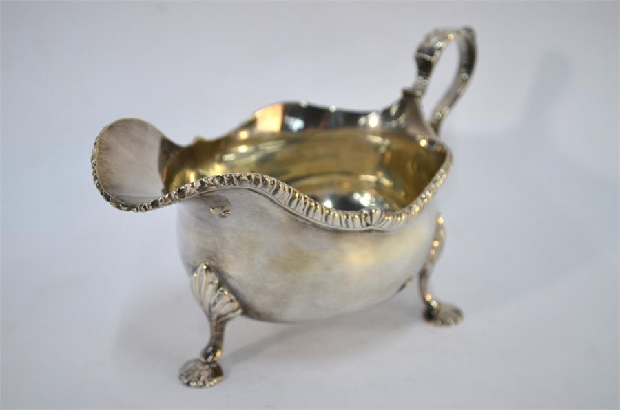 A George V silver sauce boat with scroll handle and shaped gadrooned rim, on three shell feet,