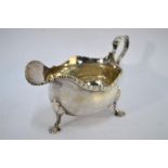 A George V silver sauce boat with scroll handle and shaped gadrooned rim, on three shell feet,