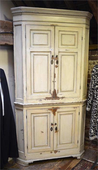 An antique painted pine cream two part standing corner cupboard, with two pairs of panelled doors