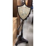 A 19th century shield shaped pole screen on turned tripod base, inset with silkwork panel