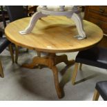 A stained pine circular dining table on a turned column and triform supports