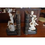 A pair of bookends formed to resemble pair of volumes flanked by Parian style figures of putti