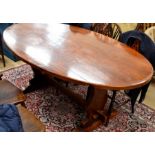 A stained oak oval drop leaf refectory table raised on shaped trestle supports with central