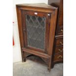 A stained oak corner cupboard with glass door over an open under tier