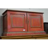 Red and green painted cupboard with a pair of panelled doors, raised on a plinth base