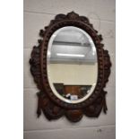 A floral and foliate carved oval oak bevelled edge wall mirror