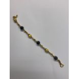 A yellow metal curb style bracelet with alternating black bead and oval bloomed yellow metal