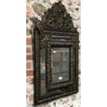 An antique continental relief cast brass decorated and ebonised bevel edged wall mirror,