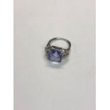 A square cushion-cut single blue stone ring, with foliate design diamond set shoulders, 9ct white