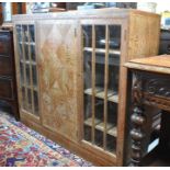 A limed oak bookcase/cabinet, centred by a chequer design door flanked by vertical glazed pane doors