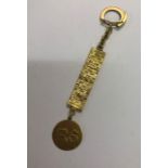 A yellow metal key ring fob, a circular disk with raised initials RS and KS on each side suspended