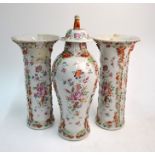A Chinese famille rose garniture comprising  three vases; one vase with a domed cover and Buddhist