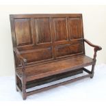 An 18th century oak settle with a six panelled back and solid seat on gun barrel front legs united