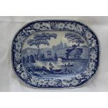 A 19th century blue and white pottery meat plate decorated with a river scene with a church beyond,