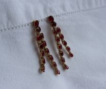 A pair of ruby and diamond drop earrings, each set with ten oval rubies,