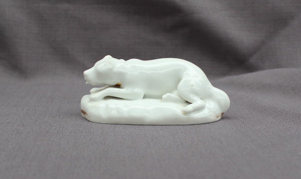 A 19th century porcelain figure of a reclining dog on an oval base,
