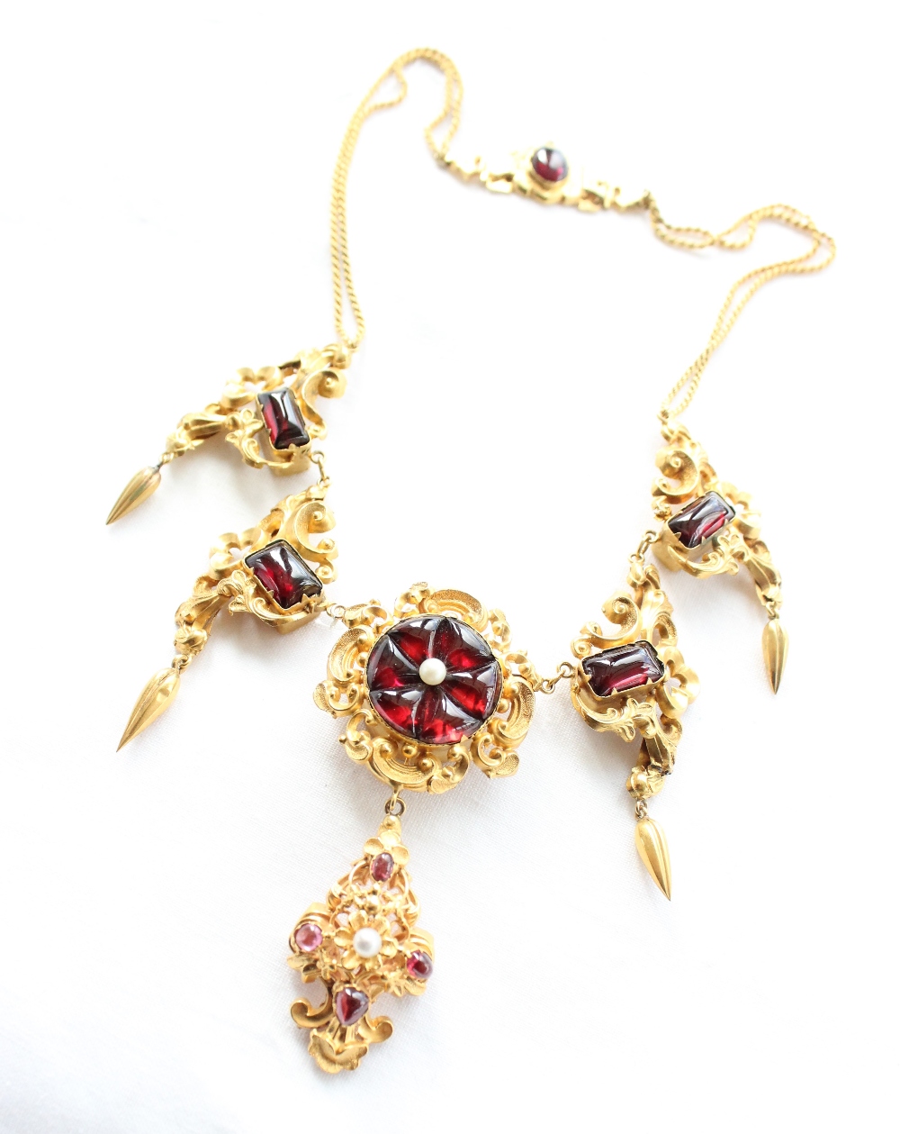 A yellow metal and red stone necklace with scrolling leaf design with pear shaped drops